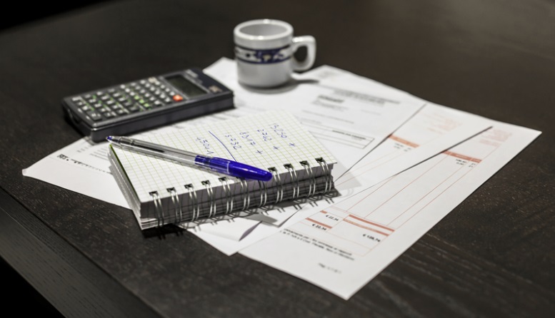 Calculator, notebook with calculations, and unpaid bills.